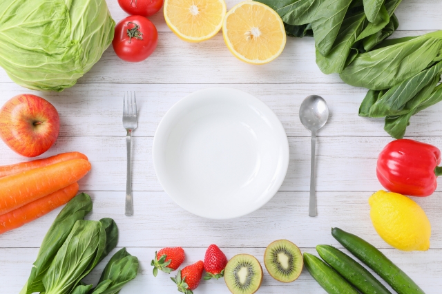 皿とフォークとスプーンと周りに色とりどりの野菜と果物